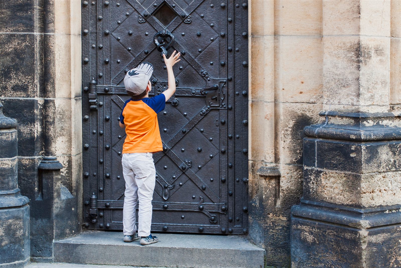 A young boy reaching up to knock on a tall wooden door